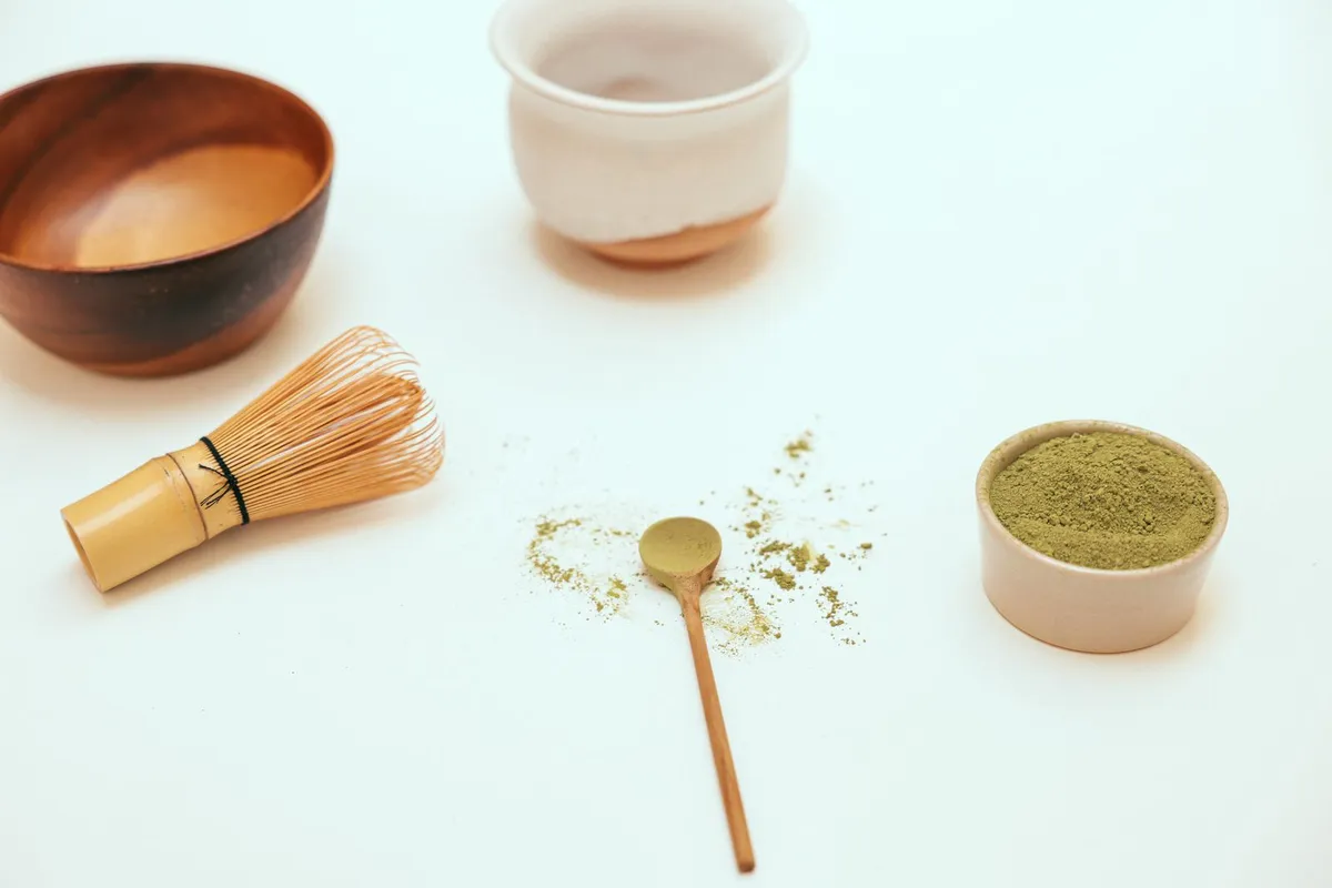 Polvo de matcha junto a un batidor chasen de bambú y utensilios
